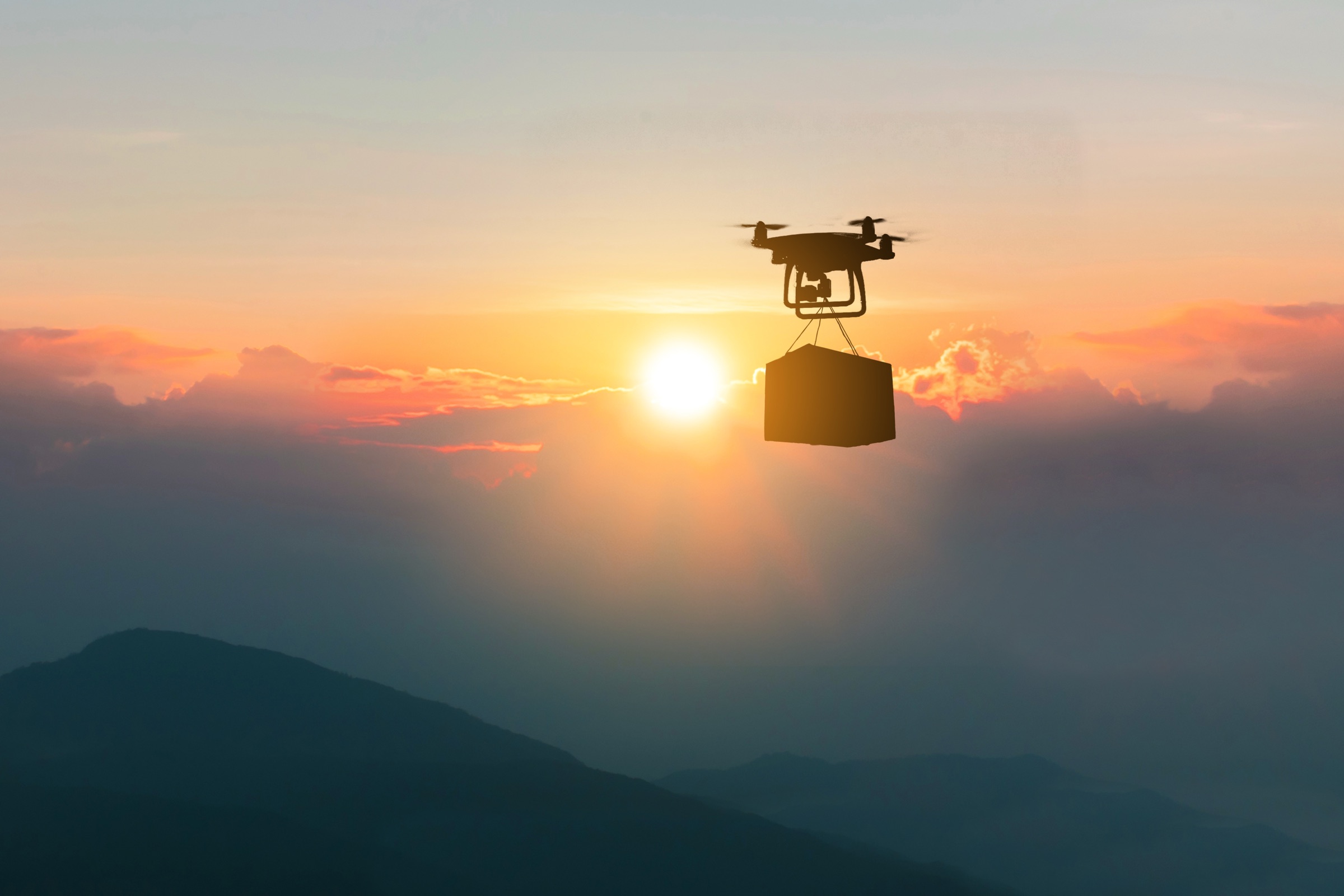 Drone silhouette carrying a package against a sunset sky