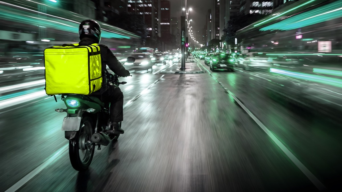 Motorcycle courier with delivery bag moving through a city at night